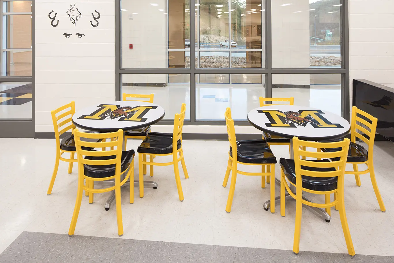 School cafeteria with round tables with the school mascot on them and chairs in the school colors, yellow and black.
